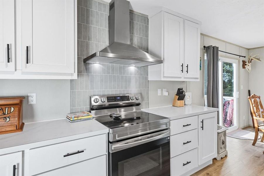 Kitchen featuring stainless steel electric range, wall chimney exhaust hood, white cabinets, and light countertops Kitchen featuring stainless steel electric range, wall chimney exhaust hood, white cabinets, and light countertops