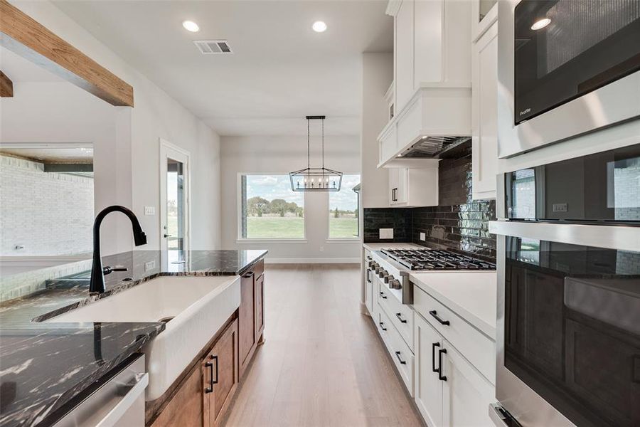Kitchen with stainless steel appliances, white cabinets, recessed lighting, dark stone counters, and hanging light fixtures