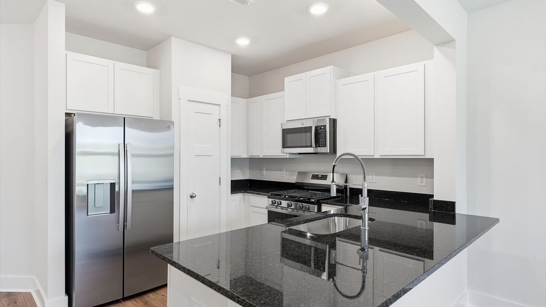 Superior craftsmanship shines in this modern kitchen with granite countertops and open flow at Clarke Townes