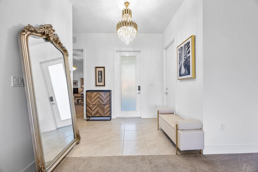 Foyer featuring light tile patterned floors, a chandelier, and light colored carpet