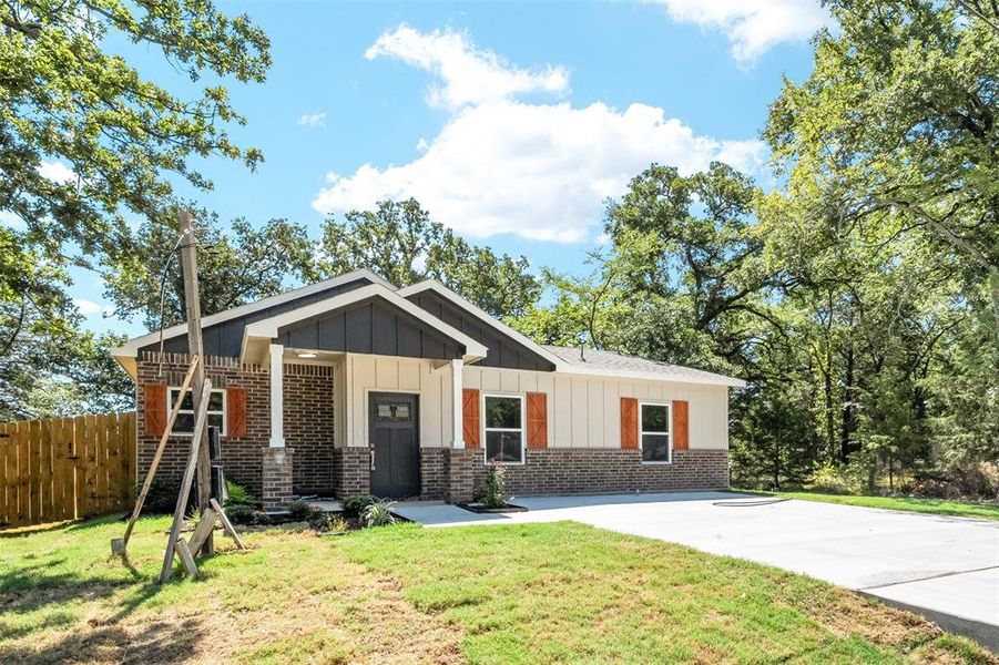 Contemporary exterior featuring brick and board-and-batten siding, a covered entry porch with columns, a dark panel door, and wood-finish window shutters Contemporary exterior featuring brick and board-and-batten siding, a covered entry porch with columns, a dark panel door, and wood-finish window shutters