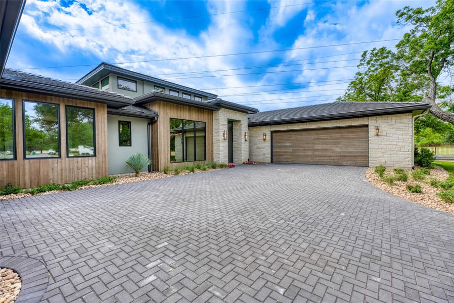 View of front of property with decorative driveway, an attached garage, and stone siding
