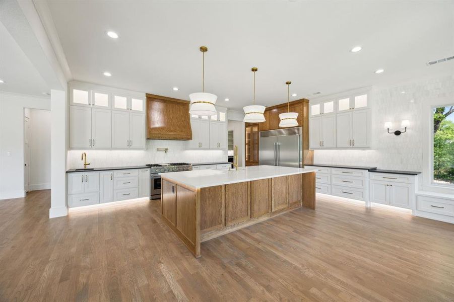 Kitchen featuring visible vents, custom exhaust hood, high quality appliances, light wood finished floors, and a spacious island Kitchen featuring visible vents, custom exhaust hood, high quality appliances, light wood finished floors, and a spacious island
