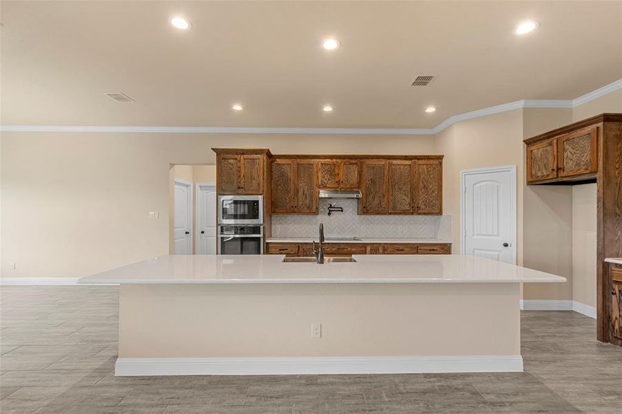Kitchen featuring built in microwave, oven, a sink, under cabinet range hood, and a large island
