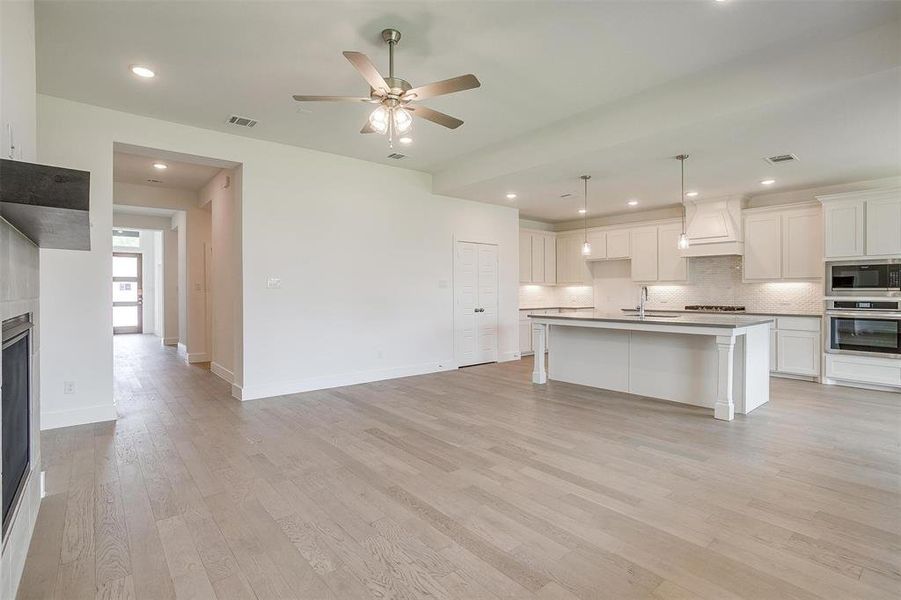 Kitchen with stainless steel appliances, a kitchen island with sink, decorative light fixtures, ceiling fan, and custom exhaust hood