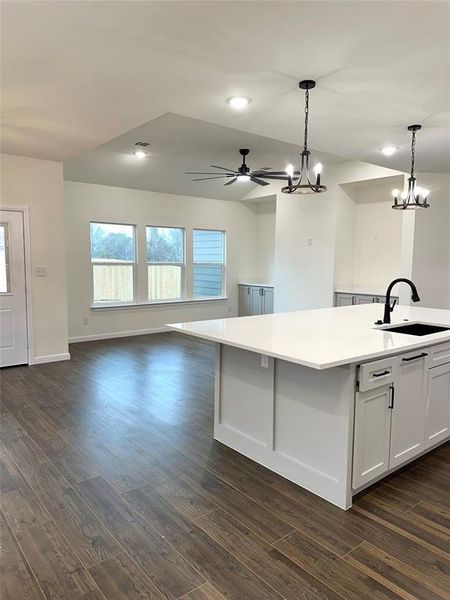 Kitchen with white cabinetry, sink, decorative light fixtures, and a center island with sink