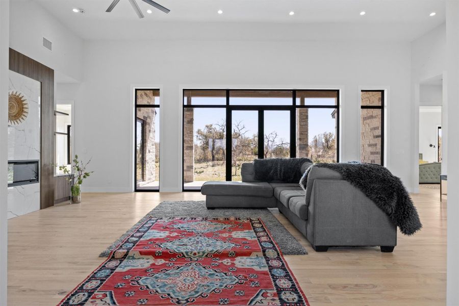 Living room with visible vents, recessed lighting, ceiling fan, light wood-style floors, and a towering ceiling