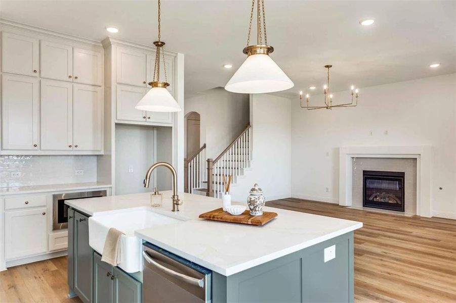 Kitchen with an island with sink, light wood-style flooring, a fireplace with flush hearth, white cabinets, and recessed lighting Kitchen with an island with sink, light wood-style flooring, a fireplace with flush hearth, white cabinets, and recessed lighting