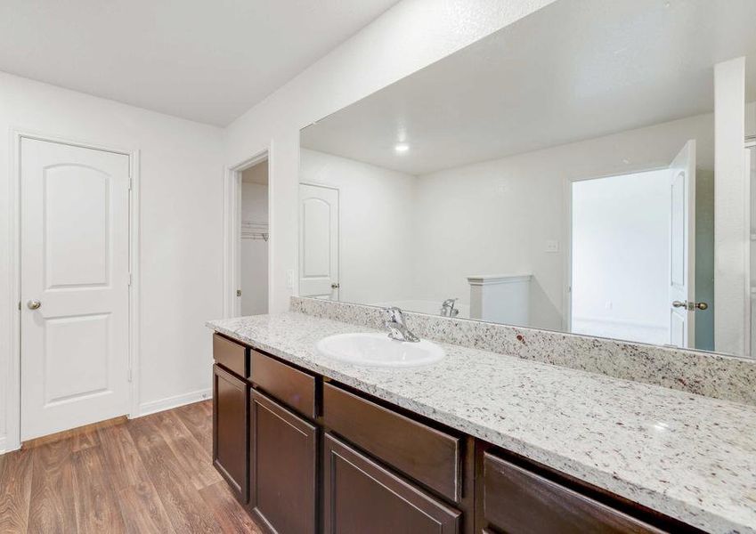 The Rio plan's master bathroom's granite countertops and dark brown cabinetry surrounded by wood-style vinyl flooring