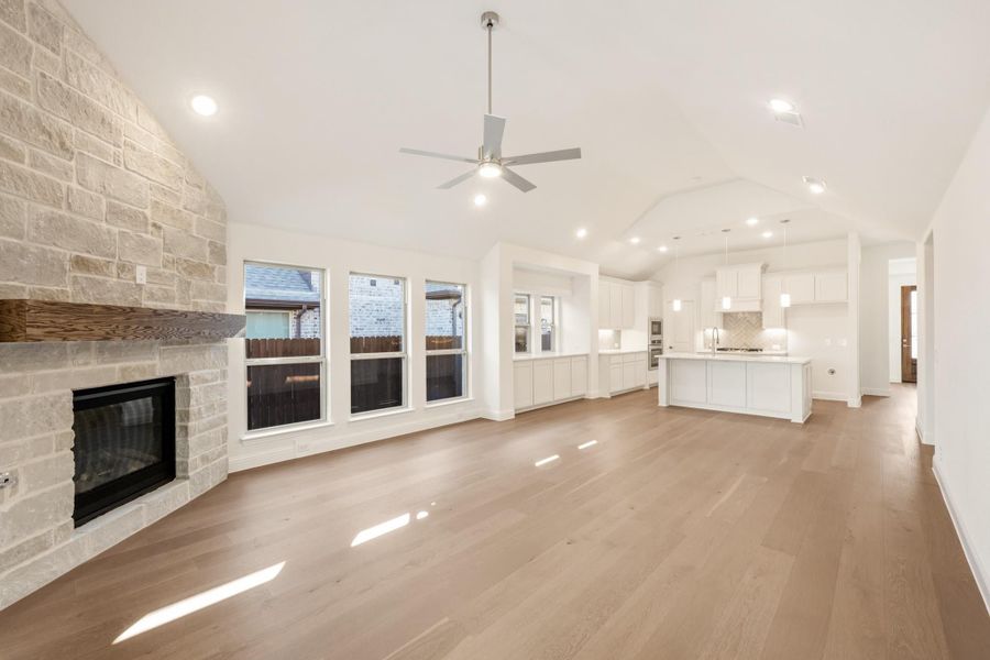 Open living area with stone fireplace, hardwood floors, vaulted ceiling, and open kitchen beyond Open living area with stone fireplace, hardwood floors, vaulted ceiling, and open kitchen beyond