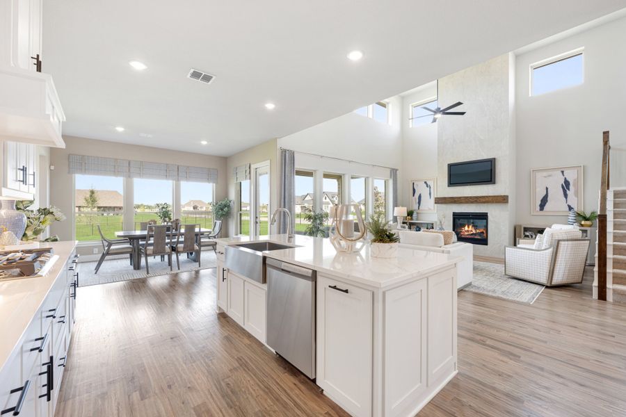 Open-concept kitchen with white island, quartz countertops, and hardwood floors flowing into living and dining areas with fireplace.