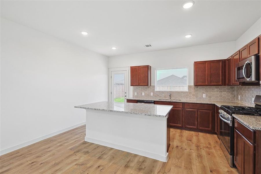 Kitchen with light stone counters, appliances with stainless steel finishes, light hardwood / wood-style floors, and a kitchen island