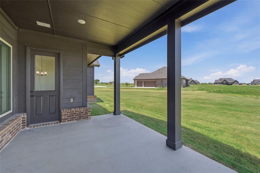 Covered concrete patio featuring dark horizontal siding and a partial brick facade Covered concrete patio featuring dark horizontal siding and a partial brick facade