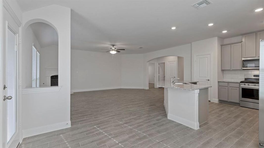 Kitchen featuring arched walkways, gray cabinets, light stone countertops, appliances with stainless steel finishes, and a center island with sink