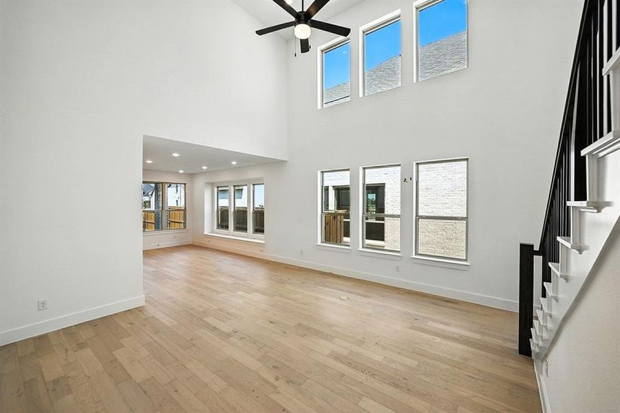 Unfurnished living room featuring light wood finished floors, stairway, a ceiling fan, and a towering ceiling Unfurnished living room featuring light wood finished floors, stairway, a ceiling fan, and a towering ceiling