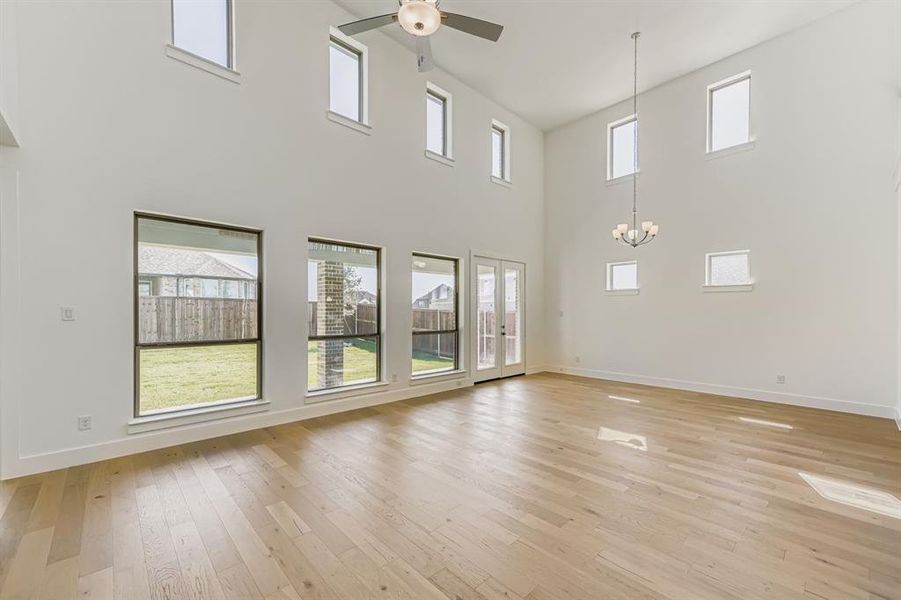 Unfurnished living room featuring light wood-style floors, plenty of natural light, a high ceiling, and ceiling fan Unfurnished living room featuring light wood-style floors, plenty of natural light, a high ceiling, and ceiling fan