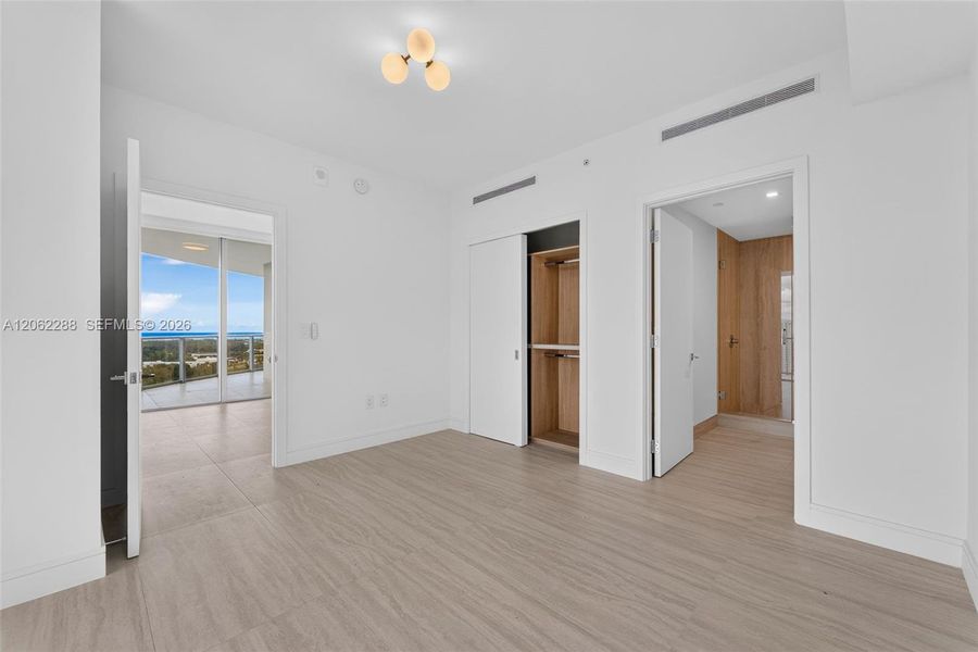 Neutral-toned tile flooring, built-in closet with interior wood finish, three-globe semi-flush mount ceiling fixture, and floor-to-ceiling glass sliding doors
