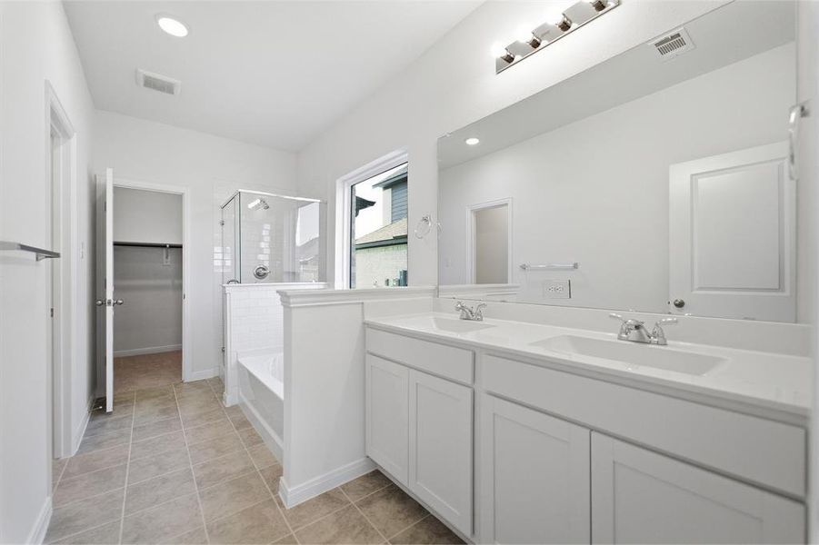 Bathroom featuring a dual-sink vanity, an integrated tub with a glass-enclosed shower, a large vanity mirror with overhead lighting, and tile flooring