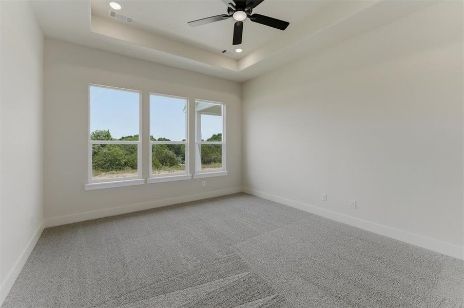 Room featuring three large windows, a tray ceiling with recessed lighting, a ceiling fan, and light grey carpeting