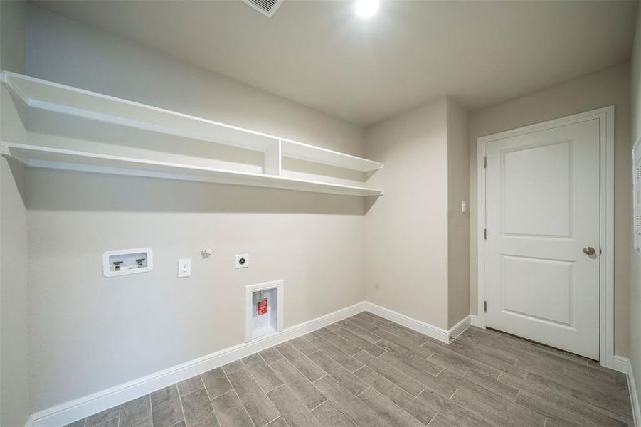 Laundry area with washer hookup, wood look tile floors, electric dryer hookup, and hookup for a electric dryer.  Door to garage