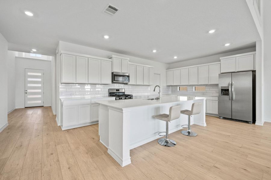 Kitchen with appliances with stainless steel finishes, a breakfast bar, backsplash, white cabinetry, and light wood-style flooring