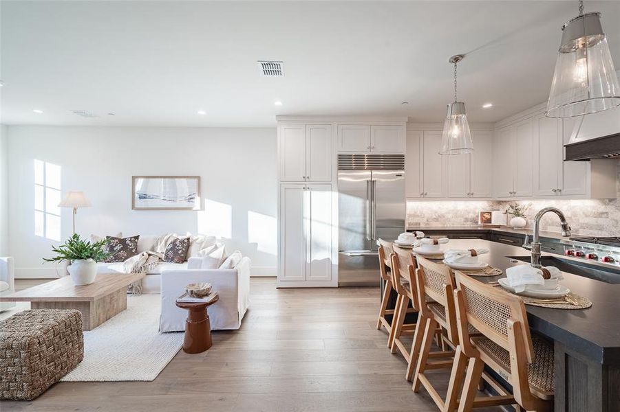 Kitchen featuring pendant lighting, sink, white cabinets, built in refrigerator, and light hardwood / wood-style floors