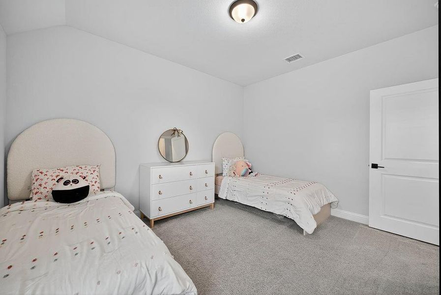 Spacious room featuring light gray carpeting, neutral wall paint, and a white paneled door with matte black hardware