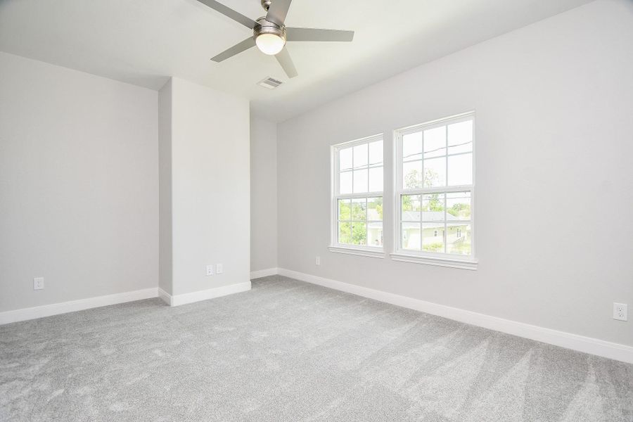 Bright, spacious room with neutral gray walls and carpet, featuring large windows for natural light and a modern ceiling fan.