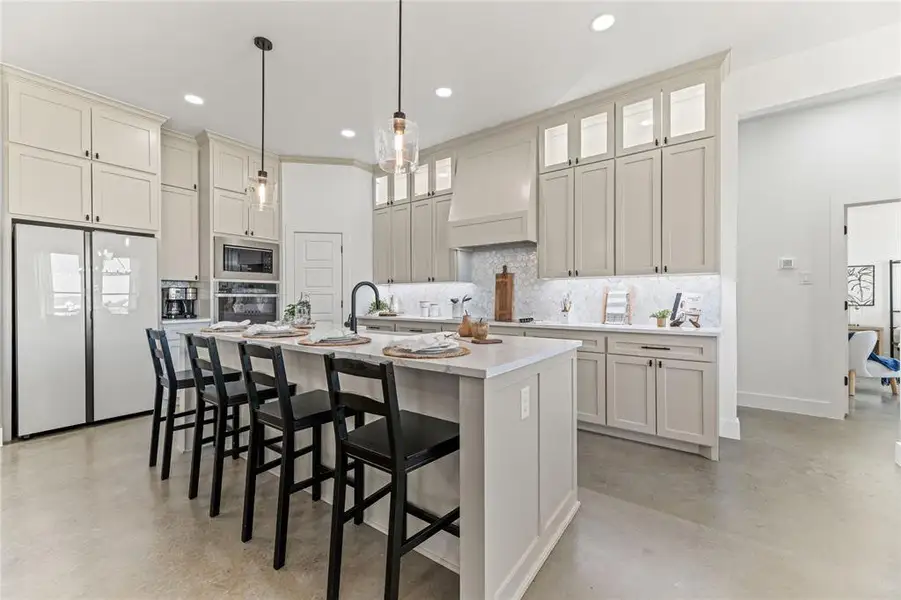 Kitchen with appliances with stainless steel finishes, concrete floors, custom range hood, tasteful backsplash, and recessed lighting Kitchen with appliances with stainless steel finishes, concrete floors, custom range hood, tasteful backsplash, and recessed lighting