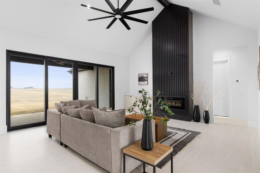 Living room featuring ceiling fan, a large fireplace, high vaulted ceiling, and light hardwood / wood-style flooring