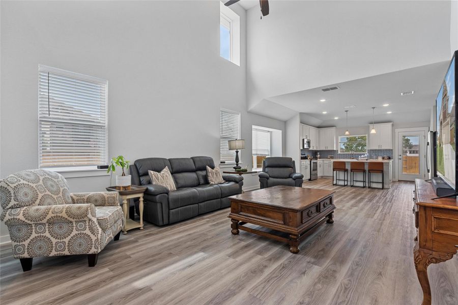 Living room featuring light wood finished floors, plenty of natural light, a high ceiling, and a ceiling fan Living room featuring light wood finished floors, plenty of natural light, a high ceiling, and a ceiling fan