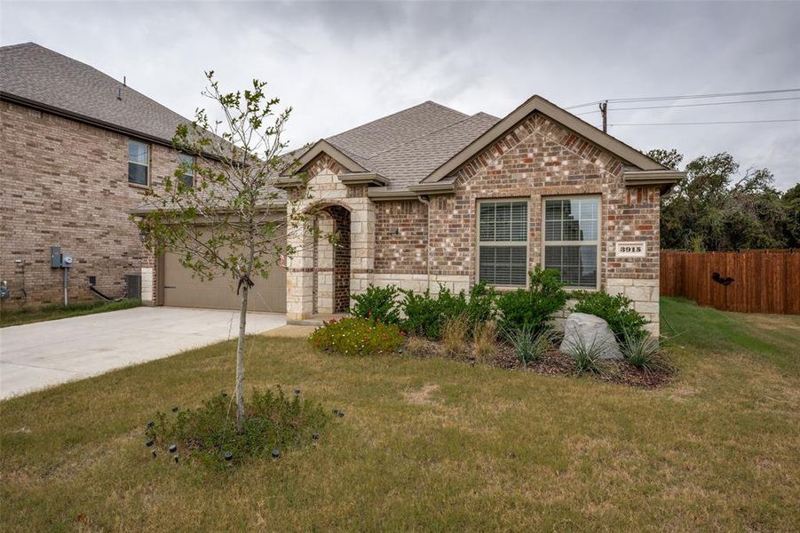 View of front facade with a shingled roof, brick siding, concrete driveway, stone siding, and a garage