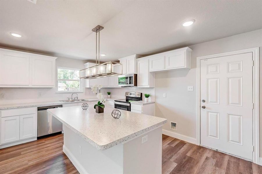 Kitchen featuring wood-type flooring, a center island, white cabinets, stainless steel appliances, and decorative light fixtures