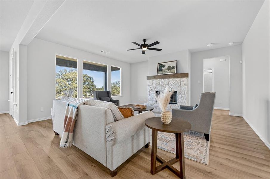 Living area featuring a stone fireplace, light wood finished floors, and a ceiling fan Living area featuring a stone fireplace, light wood finished floors, and a ceiling fan