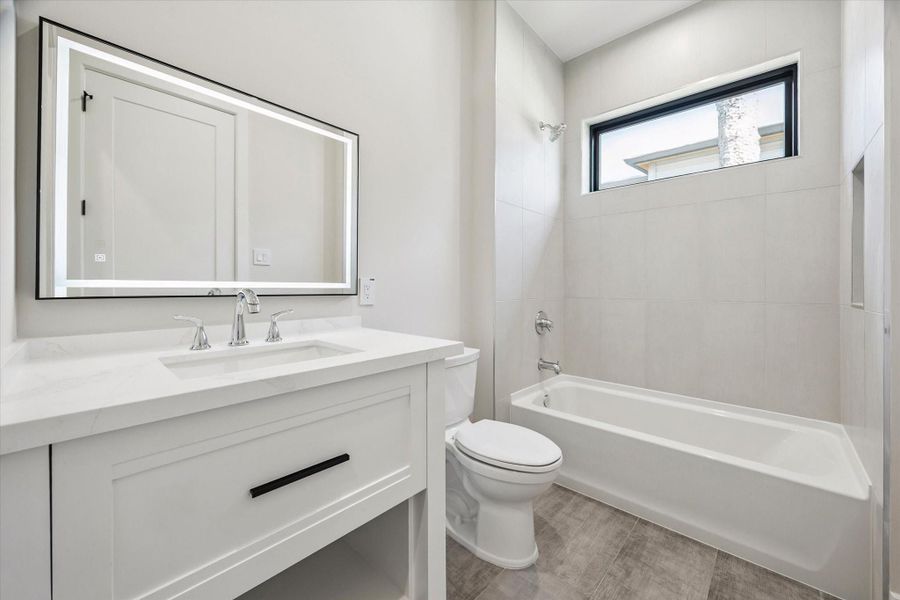 Finished with a quartz vanity and undermount sink, this bathroom includes a tub/shower combination with soap inset, offering both practicality and elegance.