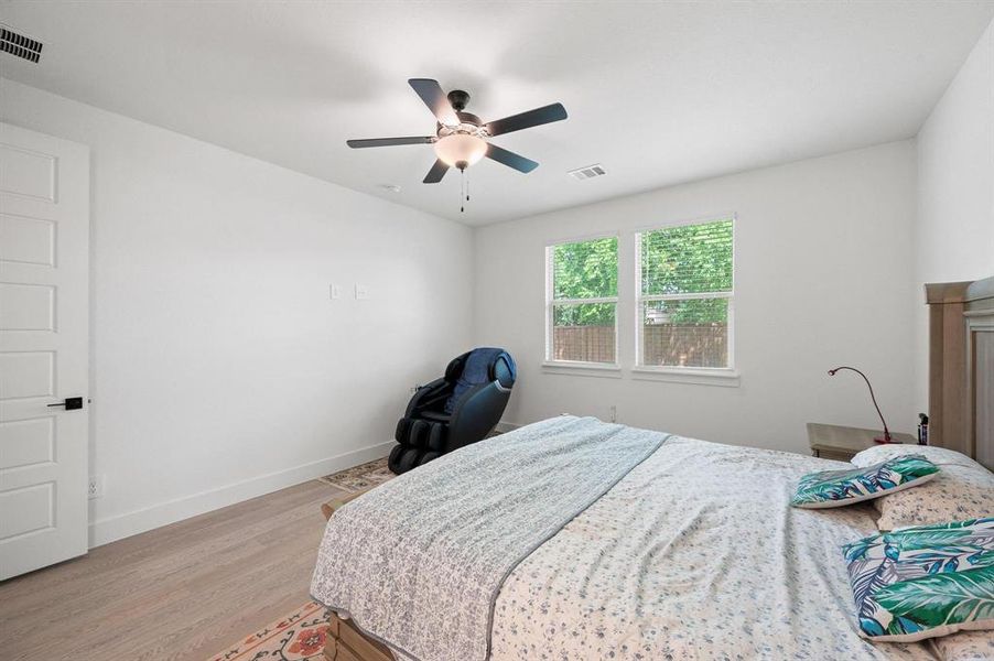 Bedroom featuring light wood-finish flooring, white trim, and a ceiling fan with integrated lighting Bedroom featuring light wood-finish flooring, white trim, and a ceiling fan with integrated lighting