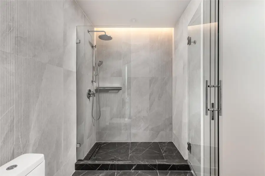 A sleek, contemporary shower enclosure features textured gray and black tile, complete with a rain showerhead and hand-held sprayer.