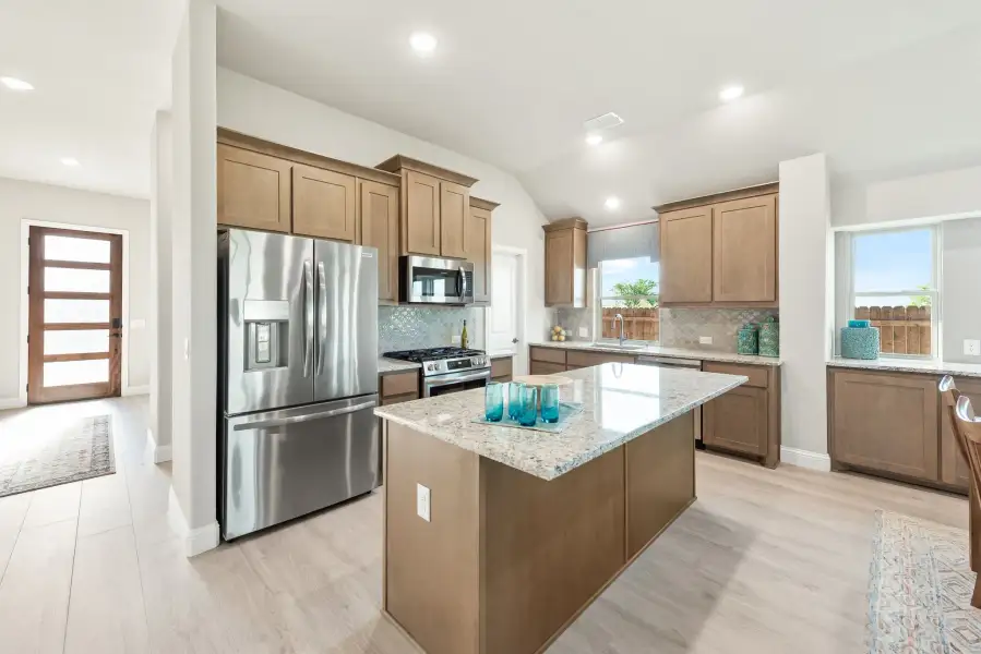 Kitchen with brown cabinets, granite island, stainless steel appliances, and light hardwood floors Kitchen with brown cabinets, granite island, stainless steel appliances, and light hardwood floors