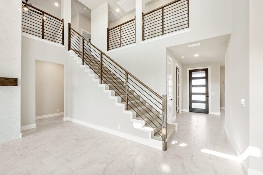 Two-story foyer with white staircase, metal railing, marble tile floors, and dark front door