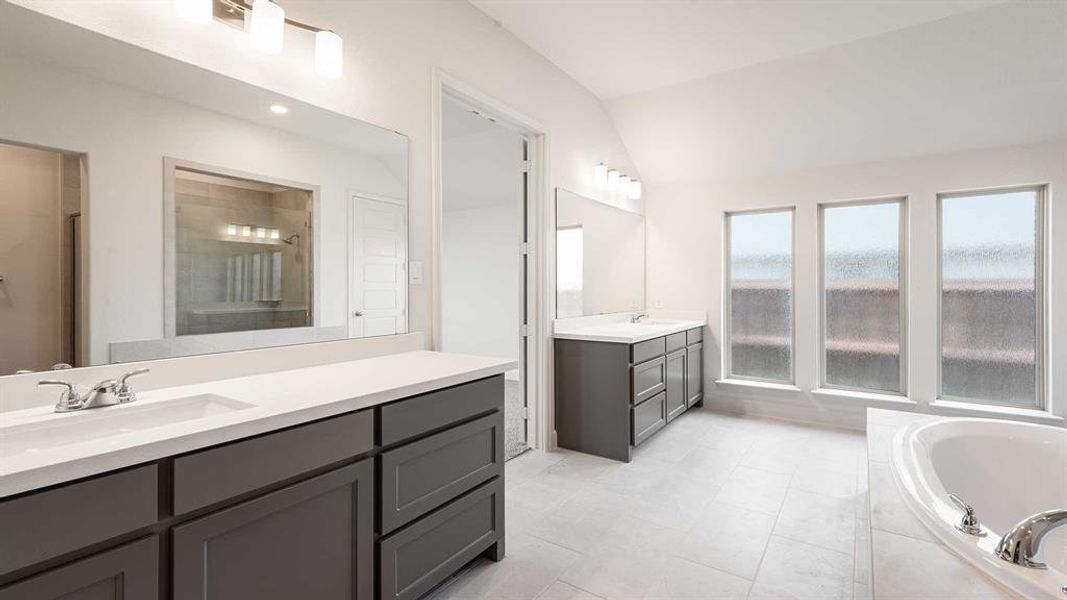 Bathroom with tile patterned floors, lofted ceiling, double vanity, and a relaxing tiled tub