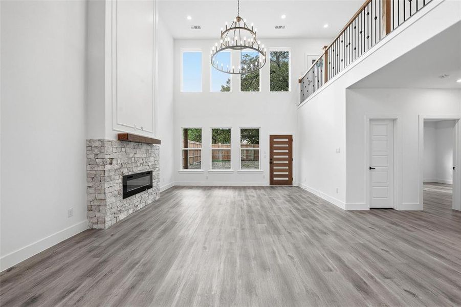 Unfurnished living room featuring a stone fireplace, a towering ceiling, light wood-style flooring, a chandelier, and recessed lighting