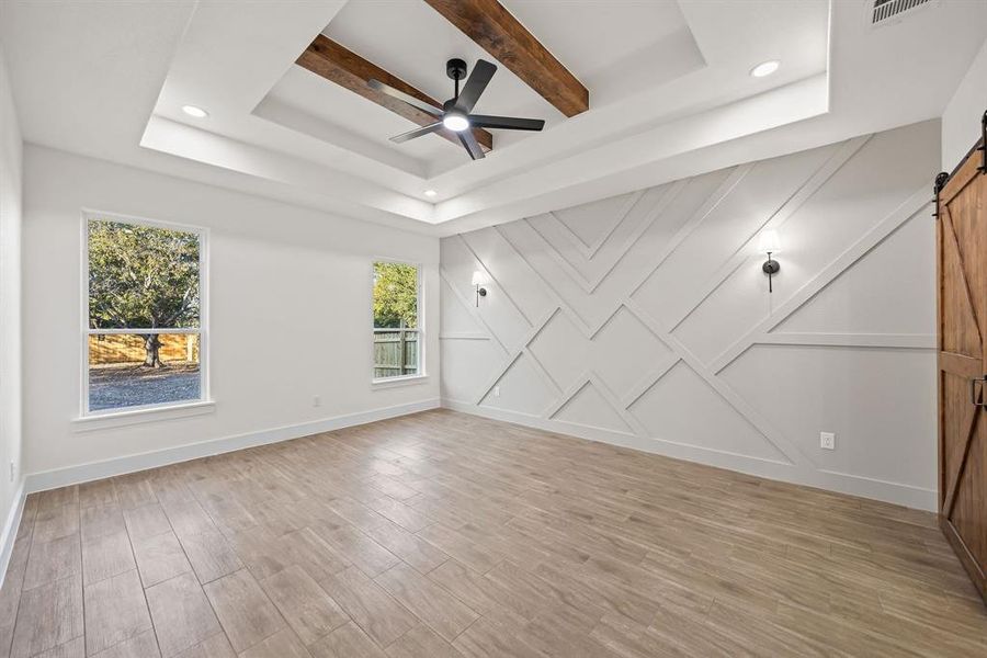 Unfurnished room featuring a barn door, a raised ceiling, light wood-style flooring, beamed ceiling, and ceiling fan