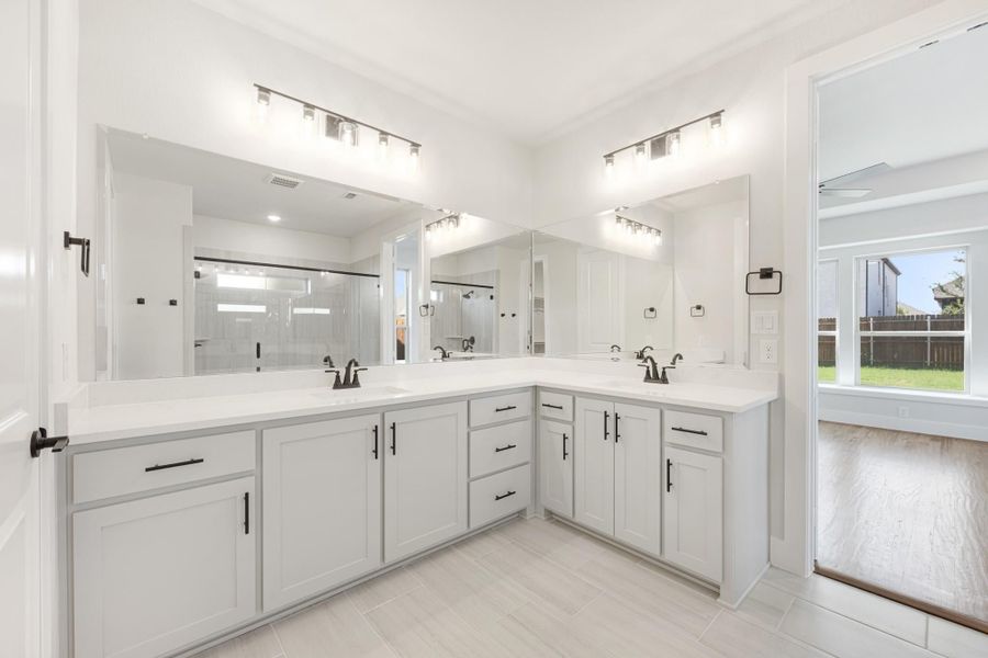 Bathroom with L-shaped double vanity, white cabinets, quartz countertops, and large mirrors above dual sinks