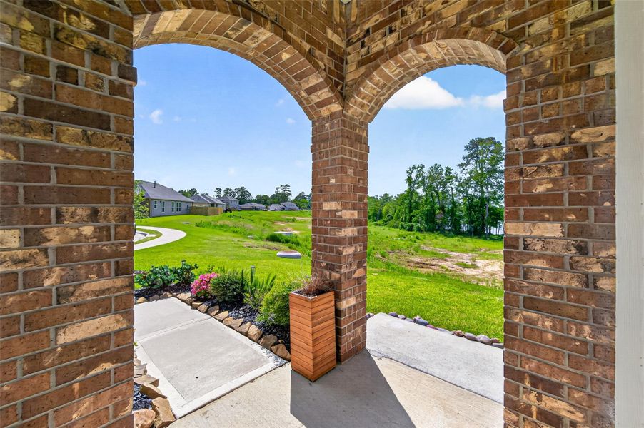 This photo showcases a charming brick porch with arched openings, overlooking a lush green yard and a peaceful neighborhood setting. Perfect for enjoying serene outdoor views. This photo showcases a charming brick porch with arched openings, overlooking a lush green yard and a peaceful neighborhood setting. Perfect for enjoying serene outdoor views.
