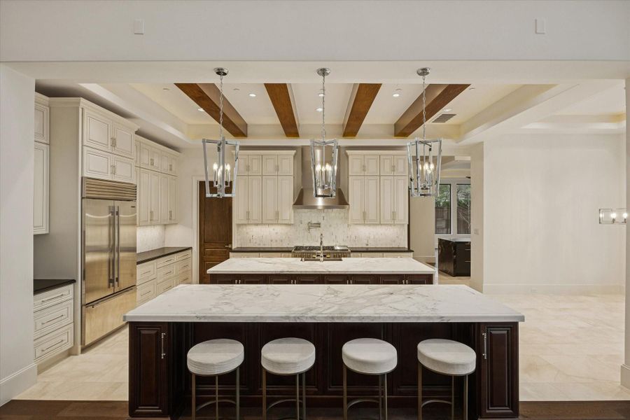 A true chef's kitchen showcasing dual oversized islands with seating, premium appliances, custom cabinetry, designer lighting, and exposed wood ceiling beams that add warmth and architectural character. A true chef's kitchen showcasing dual oversized islands with seating, premium appliances, custom cabinetry, designer lighting, and exposed wood ceiling beams that add warmth and architectural character.