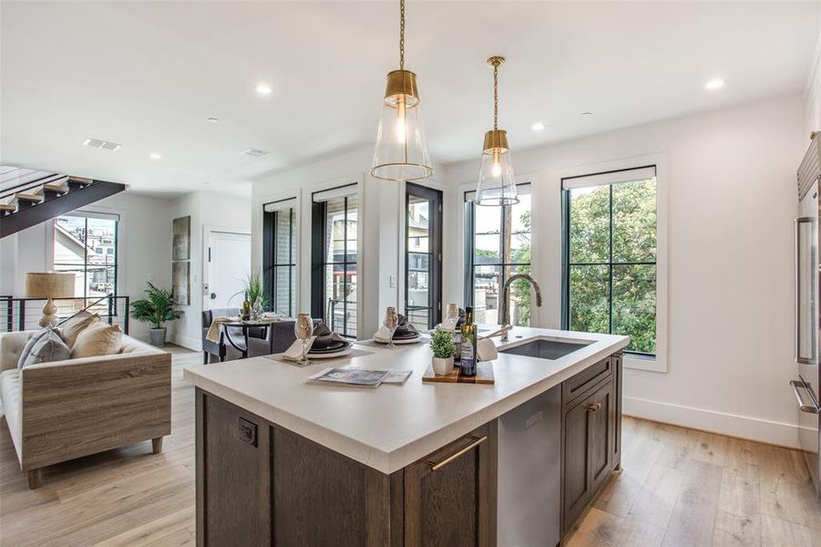 Kitchen featuring dark brown cabinetry, pendant lighting, sink, a kitchen island with sink, and light wood flooring