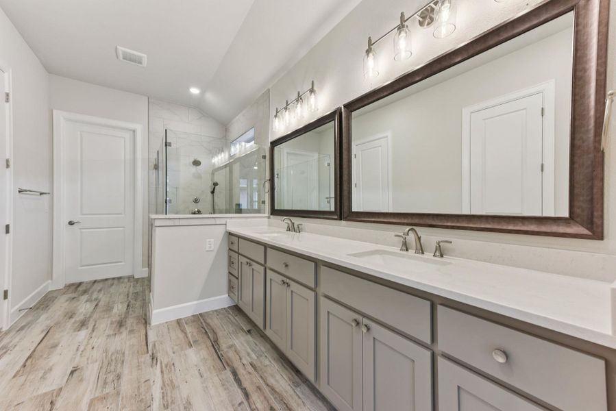 Full bathroom with double vanity, a shower stall, light wood finished floors, and recessed lighting