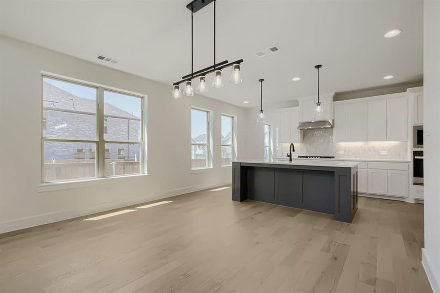 Open-concept living space featuring wood-finish flooring, a contemporary kitchen island with a light-colored countertop, recessed lighting, and ample natural light from multiple windows