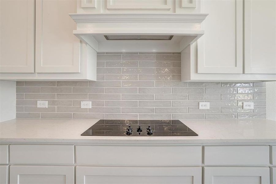 Kitchen with white cabinetry, backsplash, and black electric cooktop