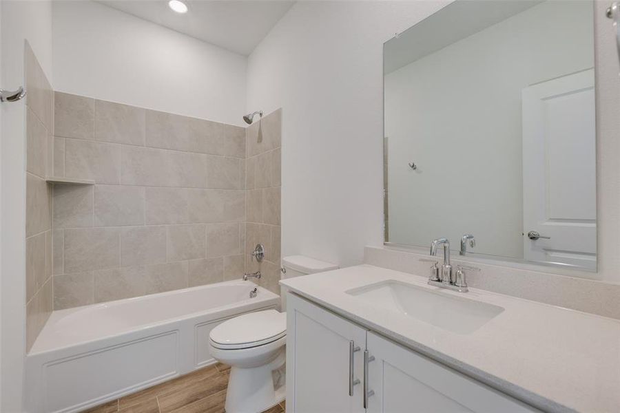 Full bathroom featuring vanity, hardwood / wood-style floors, tiled shower / bath combo, and toilet